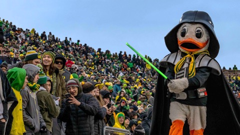 Oregon Duck dressed as Darth Vader with a light saber paraading past students at a football game